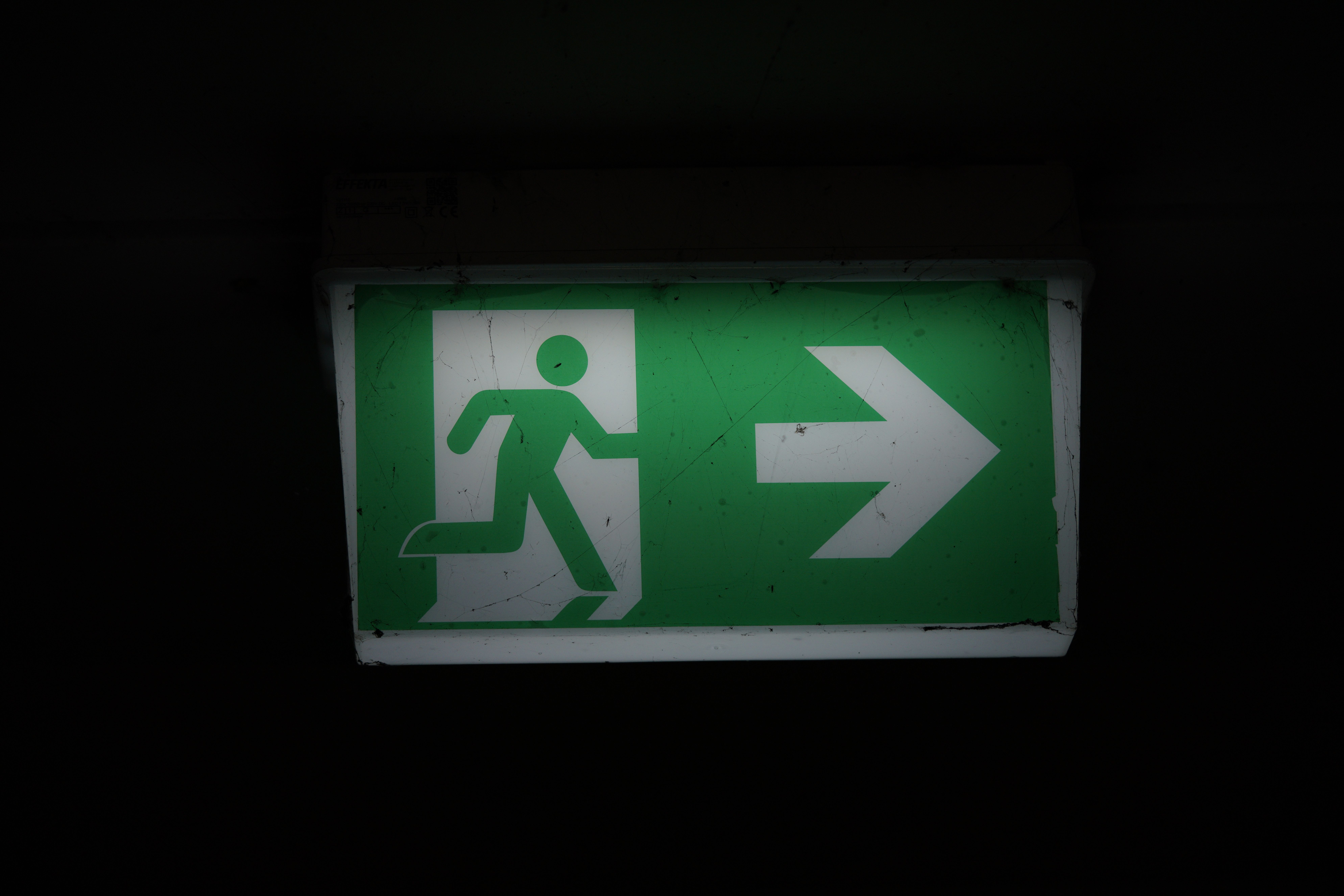 Illuminated green emergency exit sign with an arrow pointing right in a dark setting.