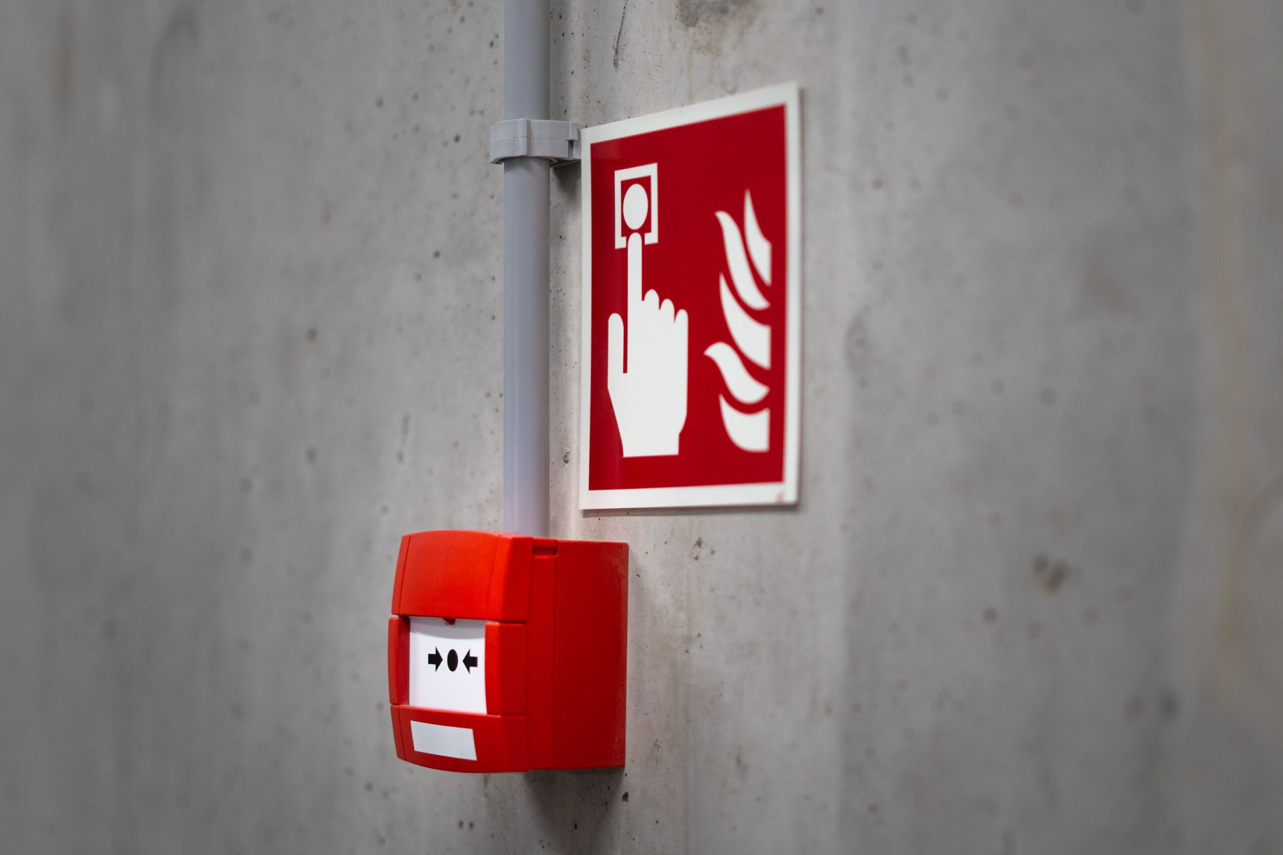 Home Red fire alarm button and sign on a concrete wall for emergency safety indoors.