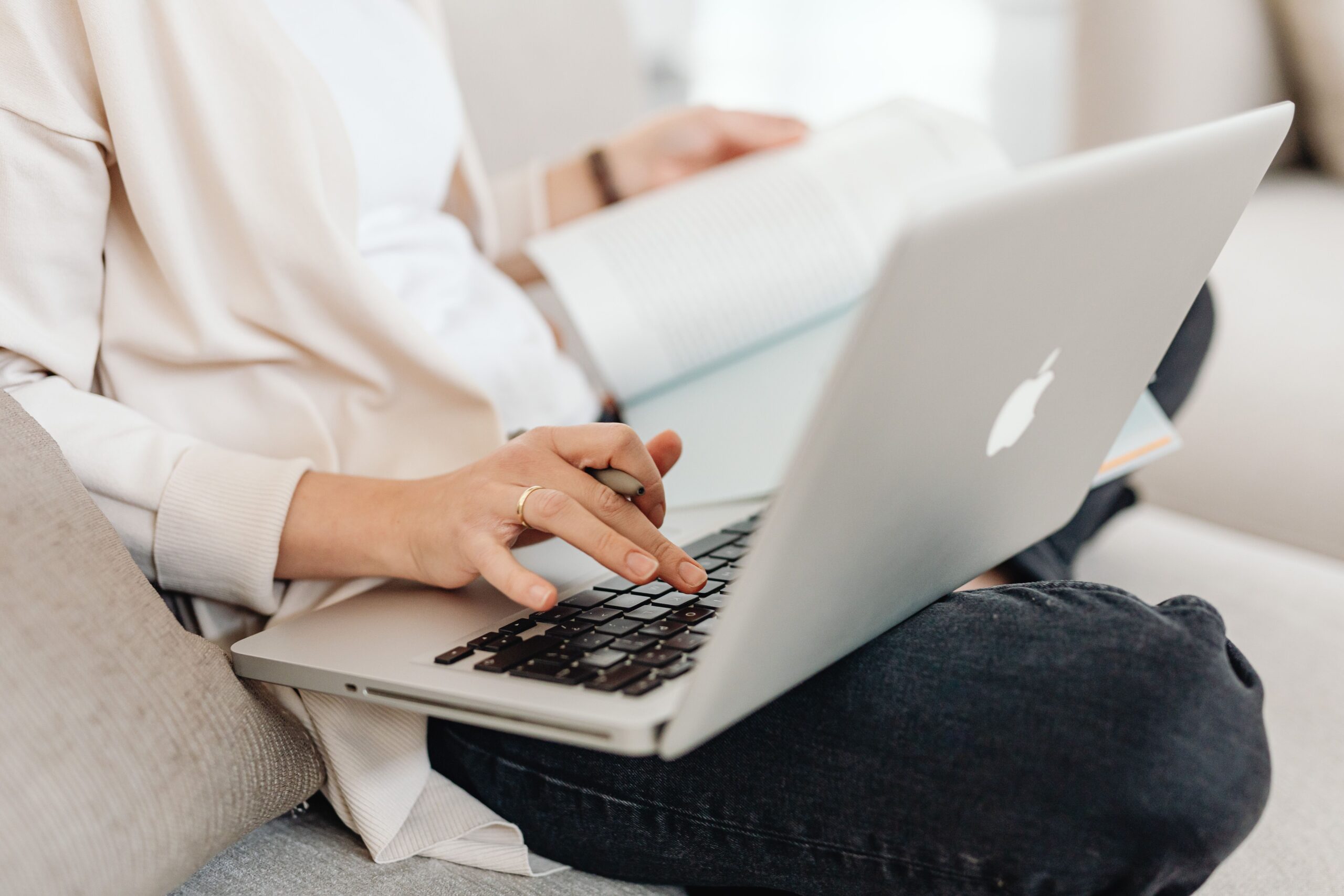 Home Close-up of a person multitasking, typing on a laptop while holding a book on their lap.